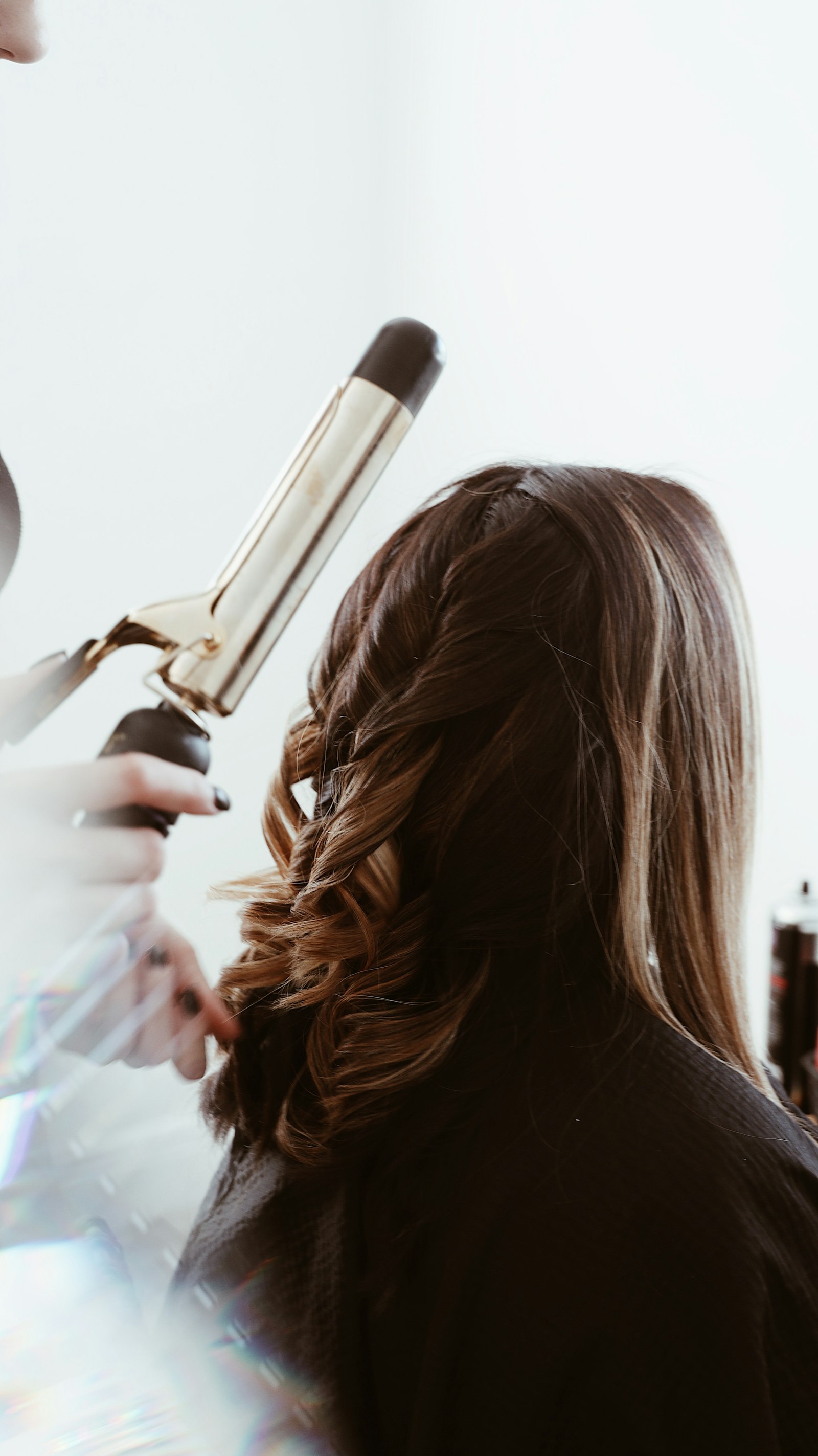 Hairstylist curling client's hair in salon